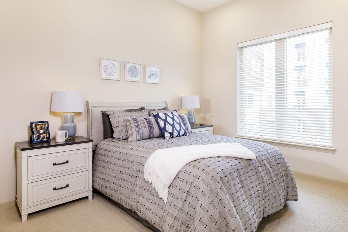 A cozy bedroom featuring a neatly made bed with patterned bedding, bedside tables with lamps, and wall artwork.