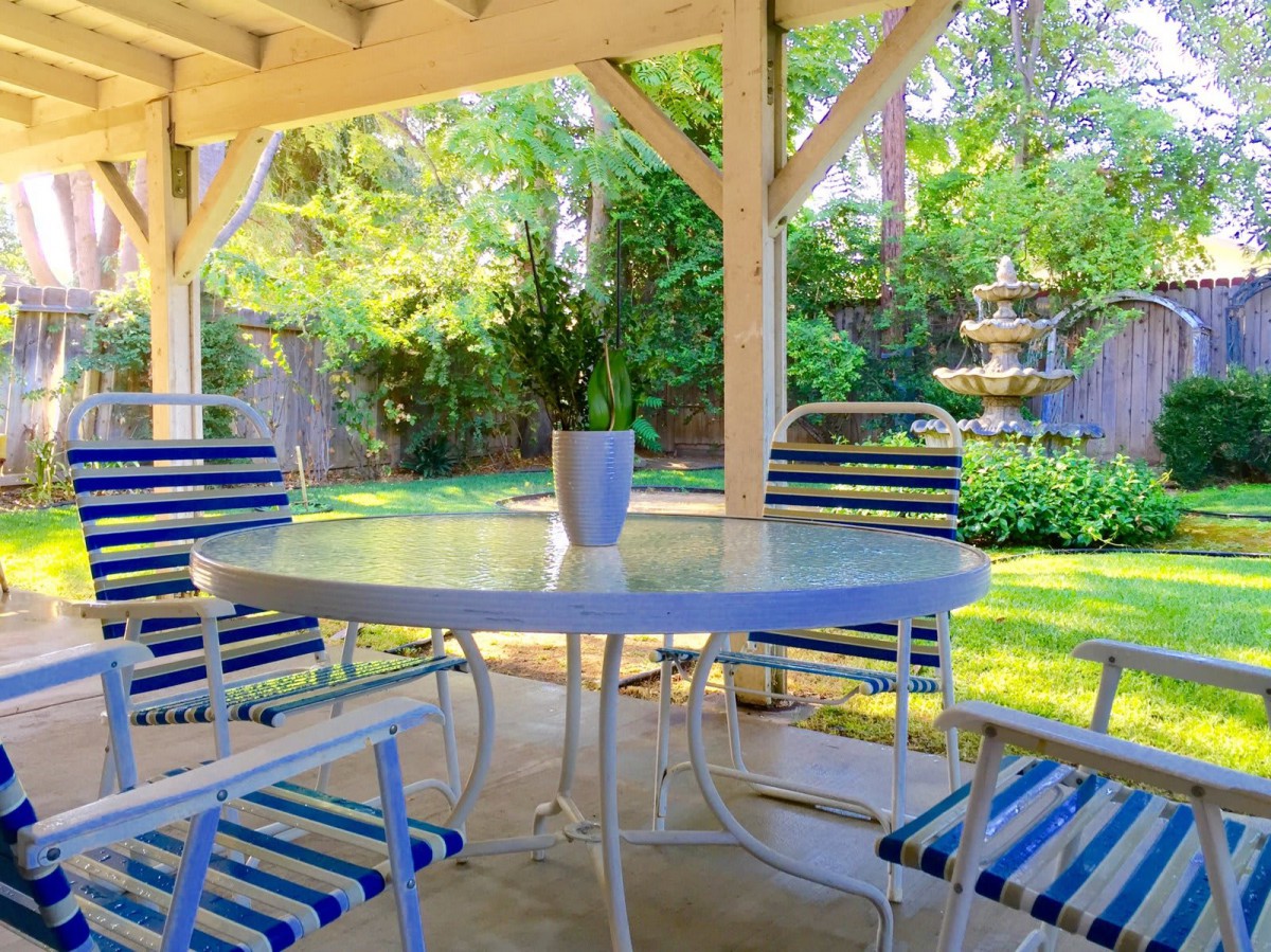 A serene backyard patio with a table and striped chairs, overlooking a lush garden.