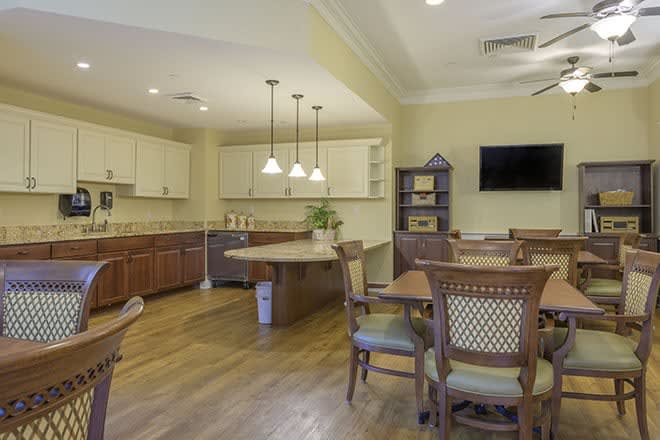 A modern kitchen and dining area featuring wooden furniture, pendant lighting, and a wall-mounted television.