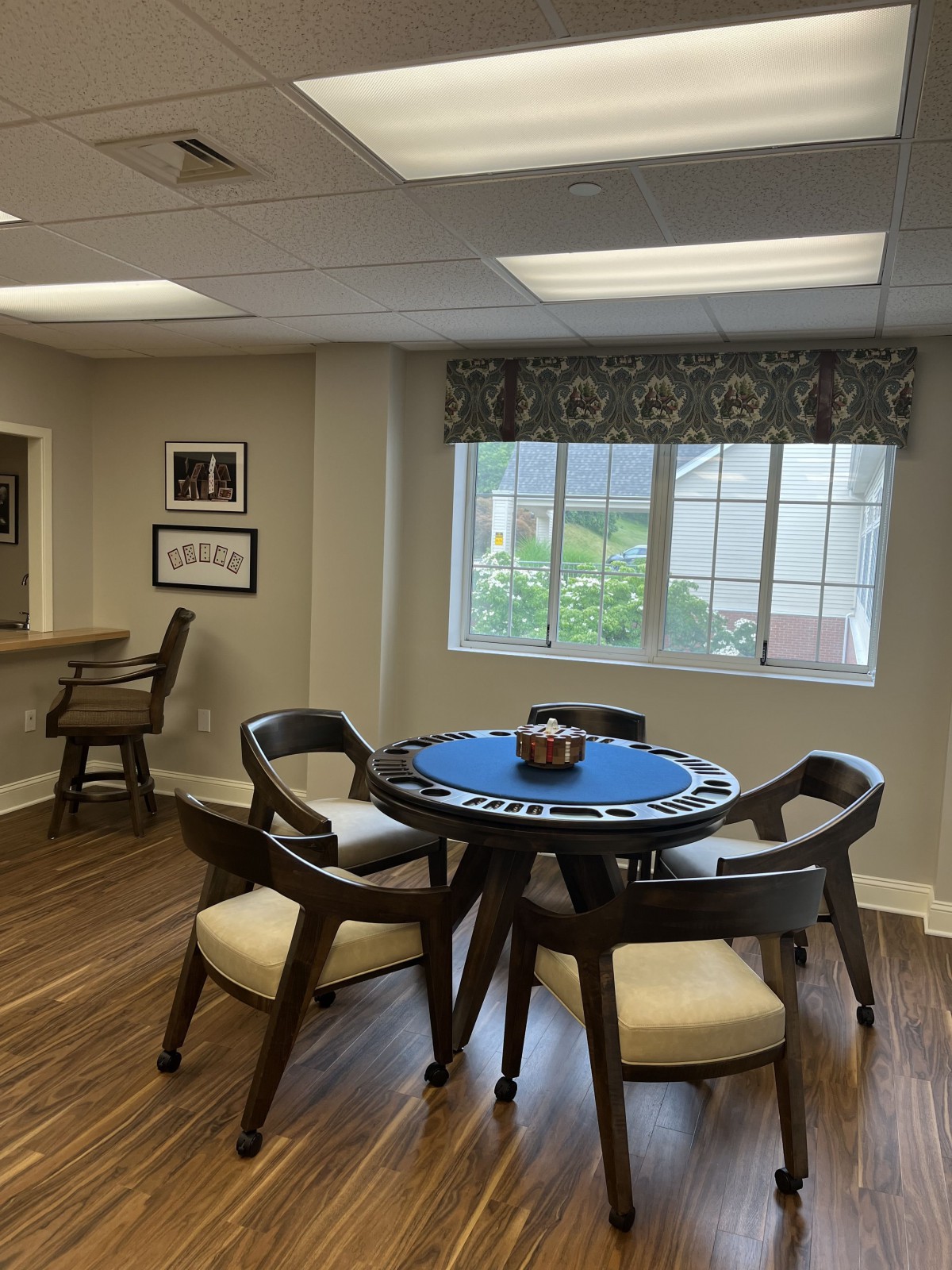 A cozy room with a round table and chairs, brightened by natural light from a large window.