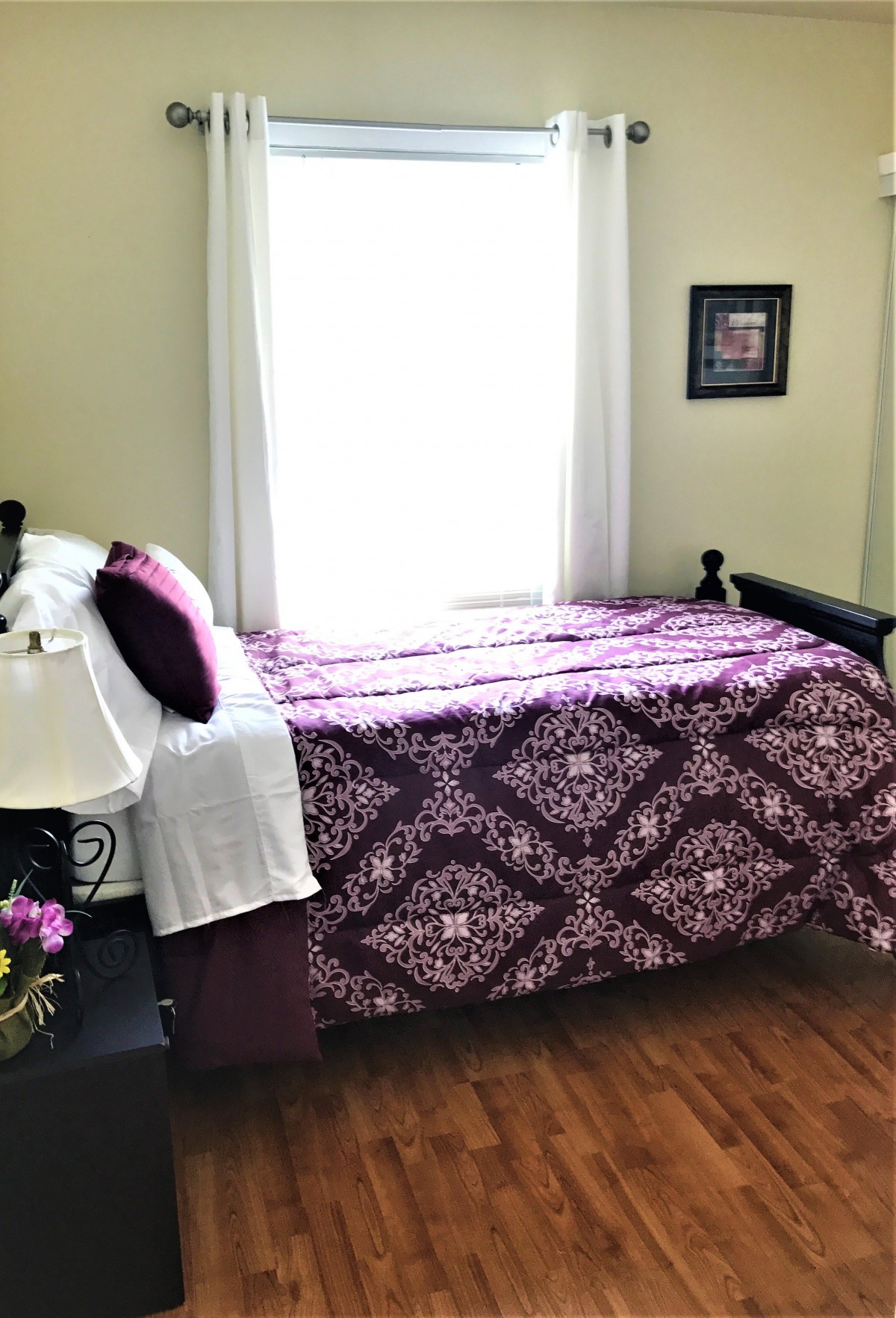 A cozy bedroom with a purple-patterned bedspread and sunlight streaming through the window.