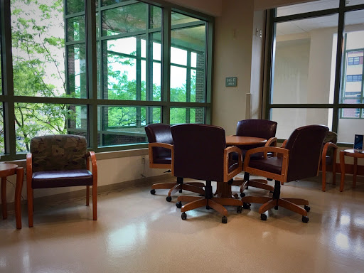 A cozy waiting area featuring comfortable chairs and a table, illuminated by natural light from large windows.