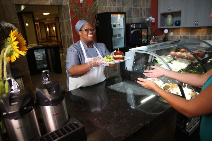 A cafeteria employee serves food to a customer at the counter.