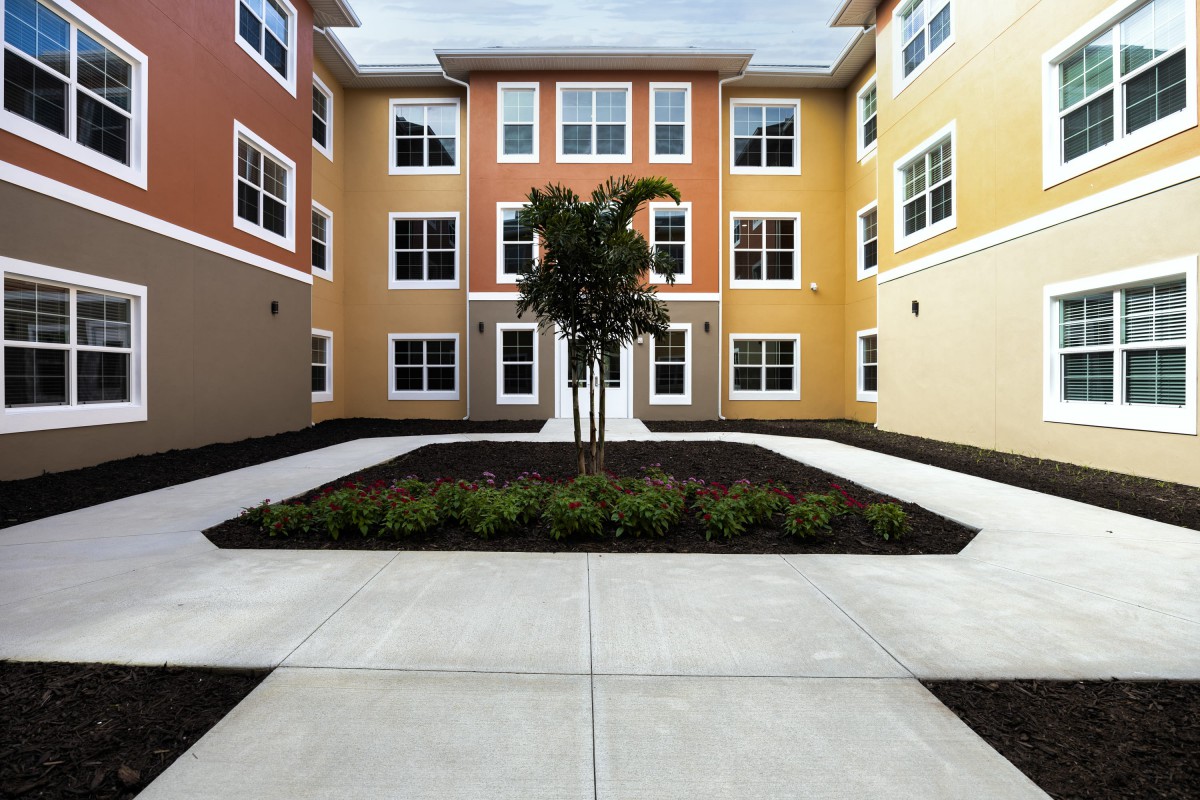 A modern three-story apartment building with a landscaped courtyard and a central palm tree.