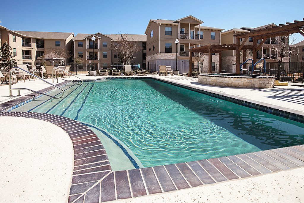 A tranquil swimming pool in an apartment complex under a clear blue sky.