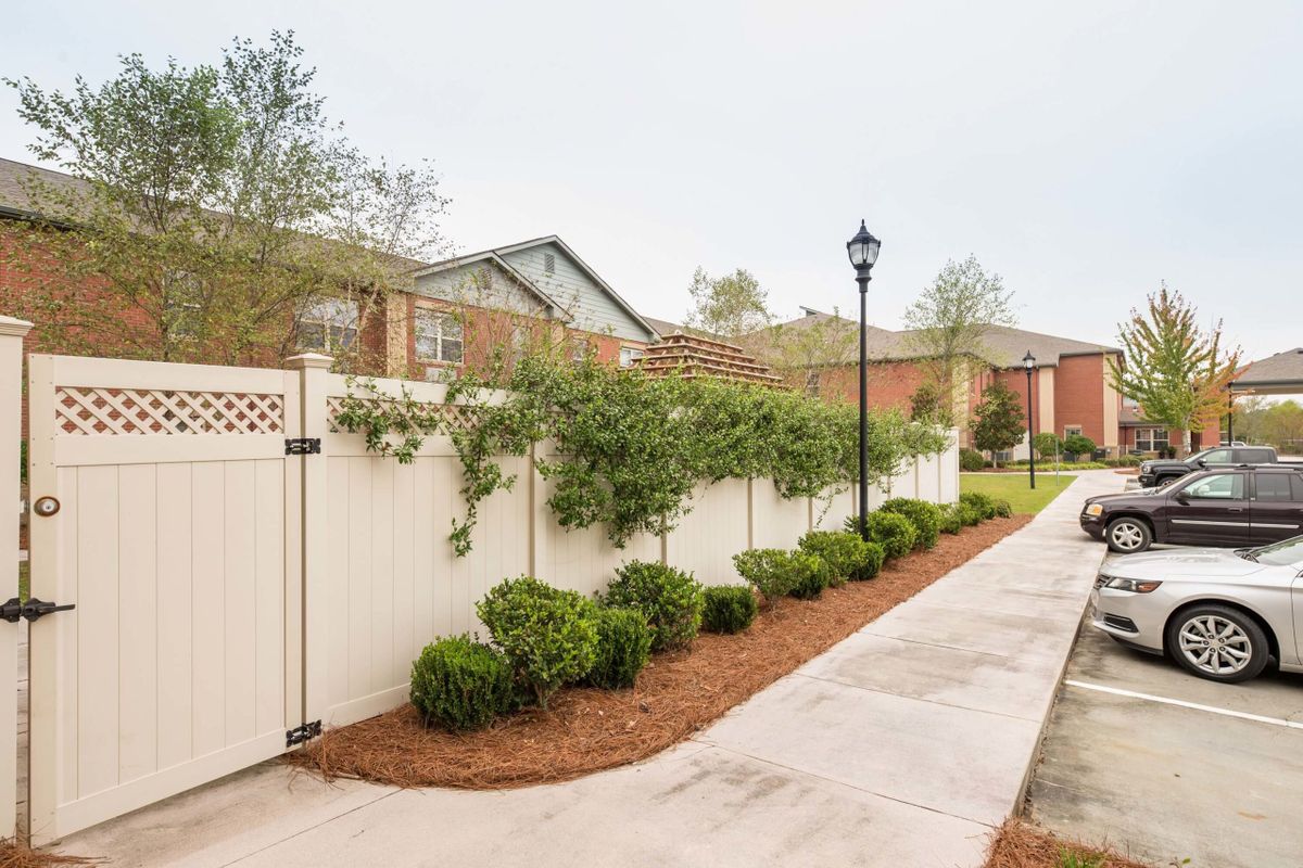 A residential area with a neatly landscaped pathway featuring shrubs and a white fence.