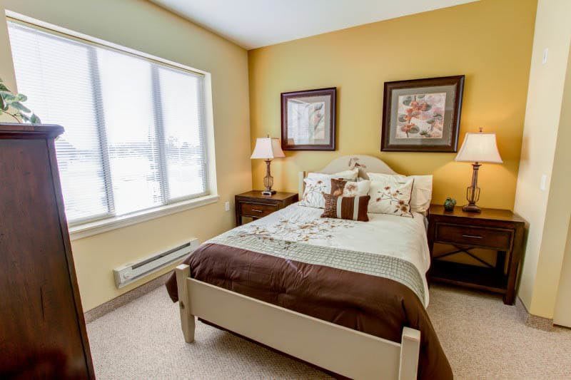 A cozy bedroom with a neatly made bed, flanked by lamps and artwork on the walls.