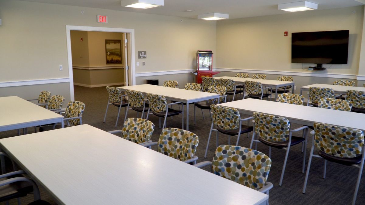 An empty meeting room with patterned chairs and white tables arranged in rows.