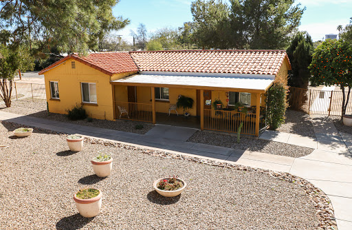 A charming yellow house with a spacious patio surrounded by gravel and potted plants.