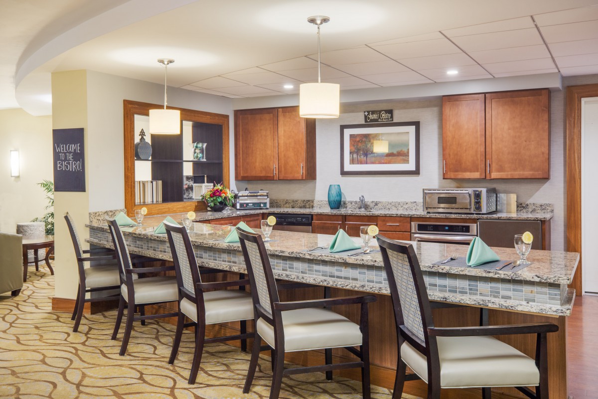 A modern kitchen and dining area featuring a long countertop with bar stools and overhead pendant lights.