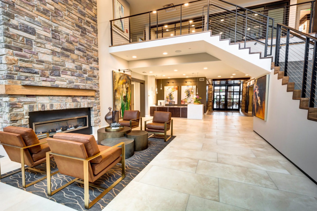 A modern lobby featuring a cozy seating area, fireplace, and reception desk, with an upper-level view accessible via stylish stairs.