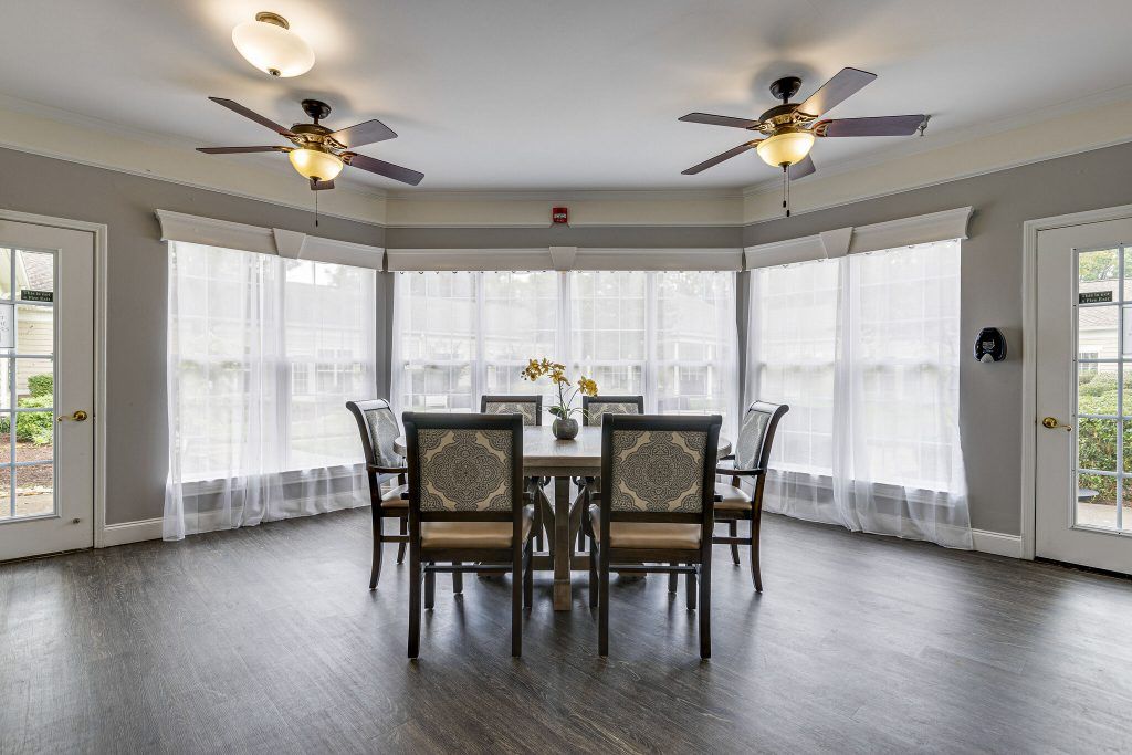 A bright dining room with a round table, six chairs, and large windows with curtains.