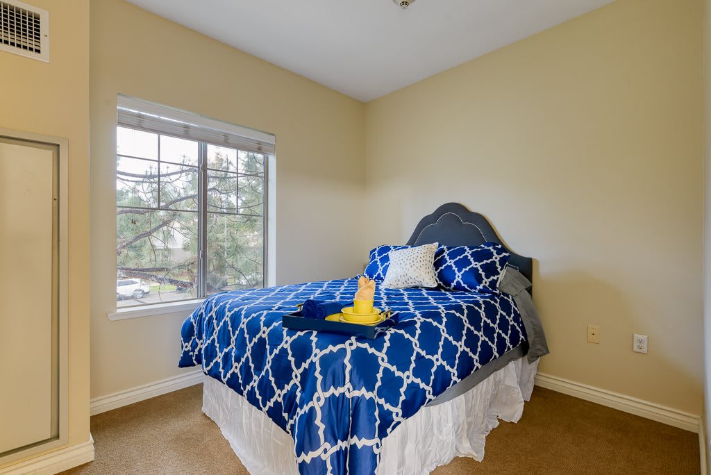 A cozy bedroom with a blue and white patterned bedspread, featuring a large window letting in natural light.