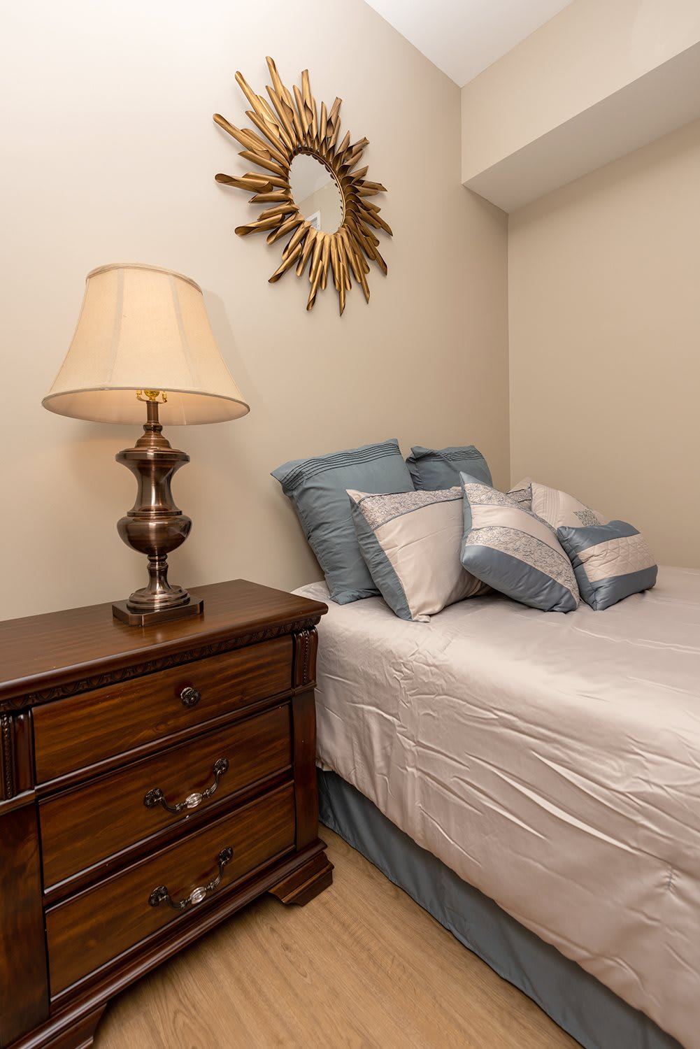 A cozy bedroom with a neatly made bed, decorative pillows, and a lamp on a wooden nightstand.