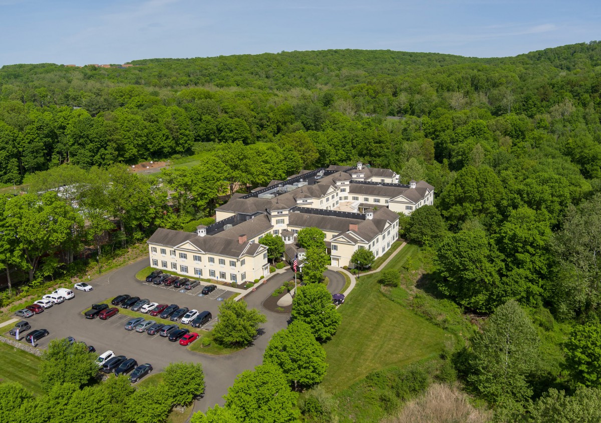 Aerial view of a large building surrounded by lush greenery and parking space.