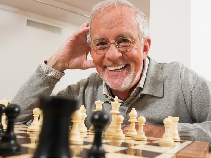 An elderly man smiling while playing chess indoors.