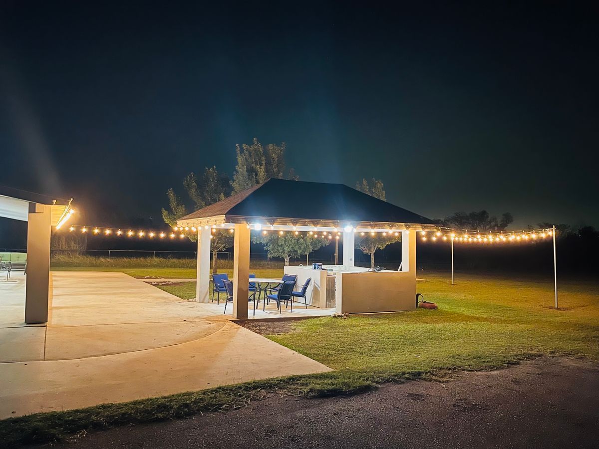 A well-lit gazebo surrounded by string lights, set on a lawn during nighttime.