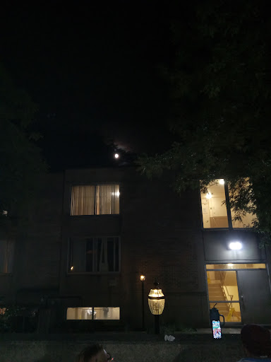 A serene night scene featuring a building illuminated by warm lights and the moon shining in the sky.