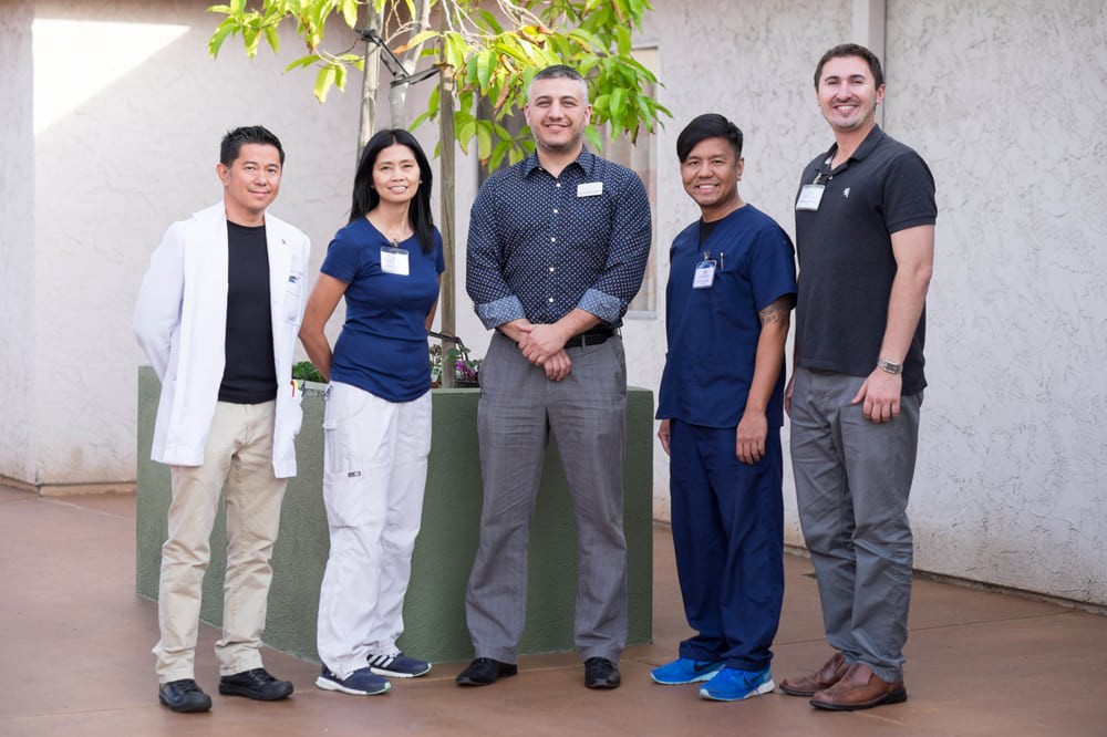 A group of five people standing together outside, dressed in both casual and professional attire.