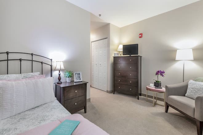 A cozy bedroom with a neatly made bed, a lamp on the nightstand, and a dresser with a television on top.