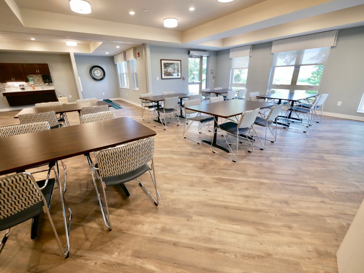 A modern dining area with tables and chairs, featuring wood flooring and ample natural light.