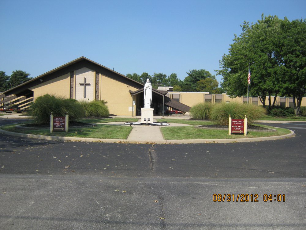 A church with a statue in front, surrounded by greenery.