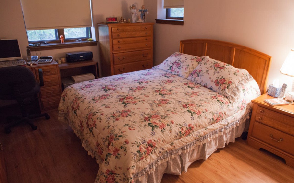 A cozy bedroom featuring a bed with floral bedding, a dresser, and a nightstand.
