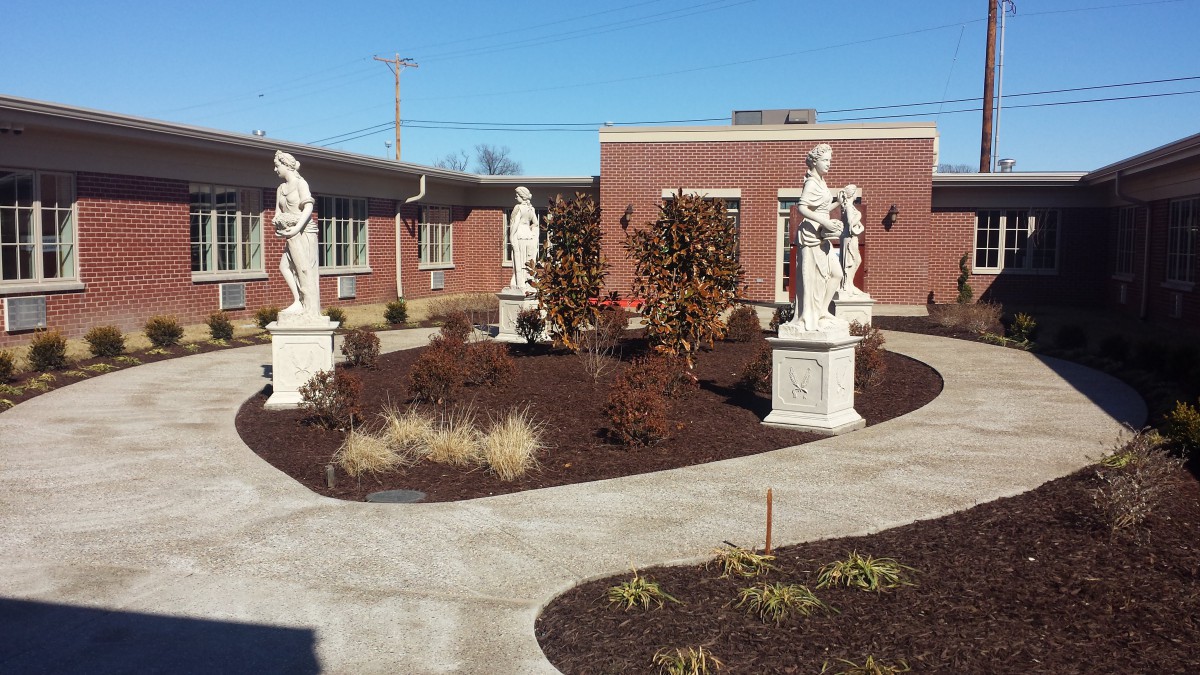 A courtyard garden with statues and a brick building in the background.