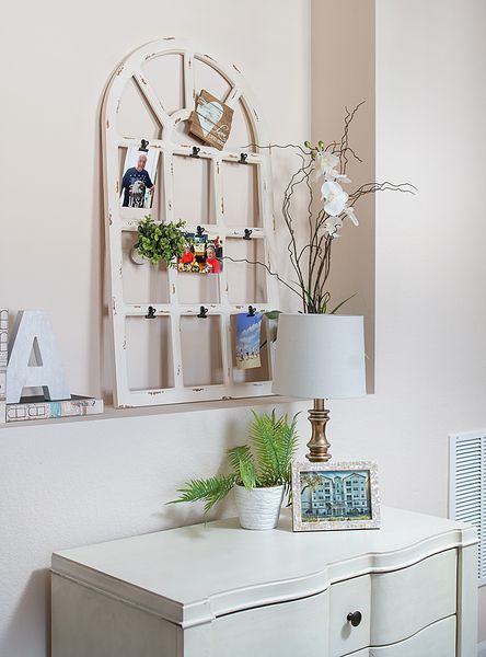 A cozy interior space featuring a decorative photo display above a desk with plants and a lamp.