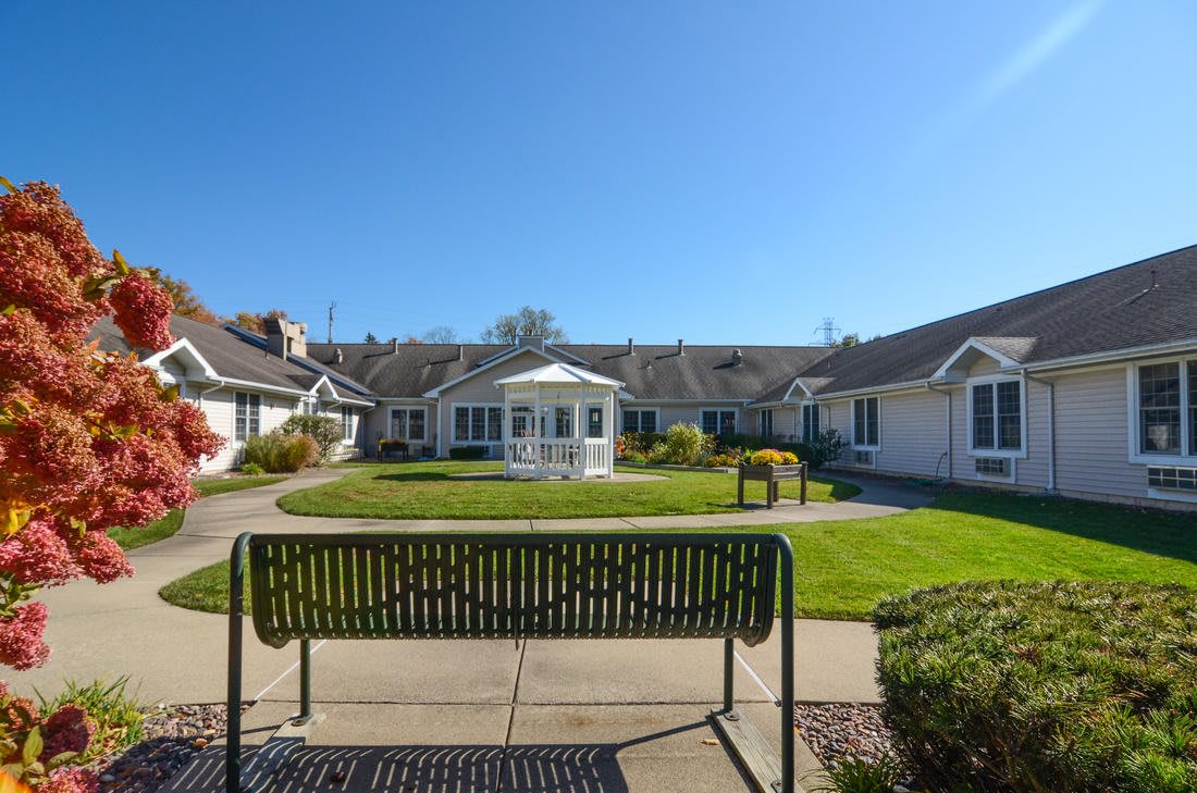 A sunny day in a serene garden with a bench facing a house.