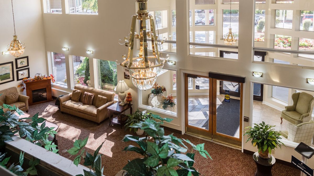 A spacious and well-lit lobby featuring a large chandelier, comfortable sofa, and lush indoor plants.