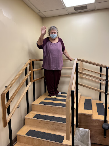 A person standing on stairs, waving while wearing a mask.