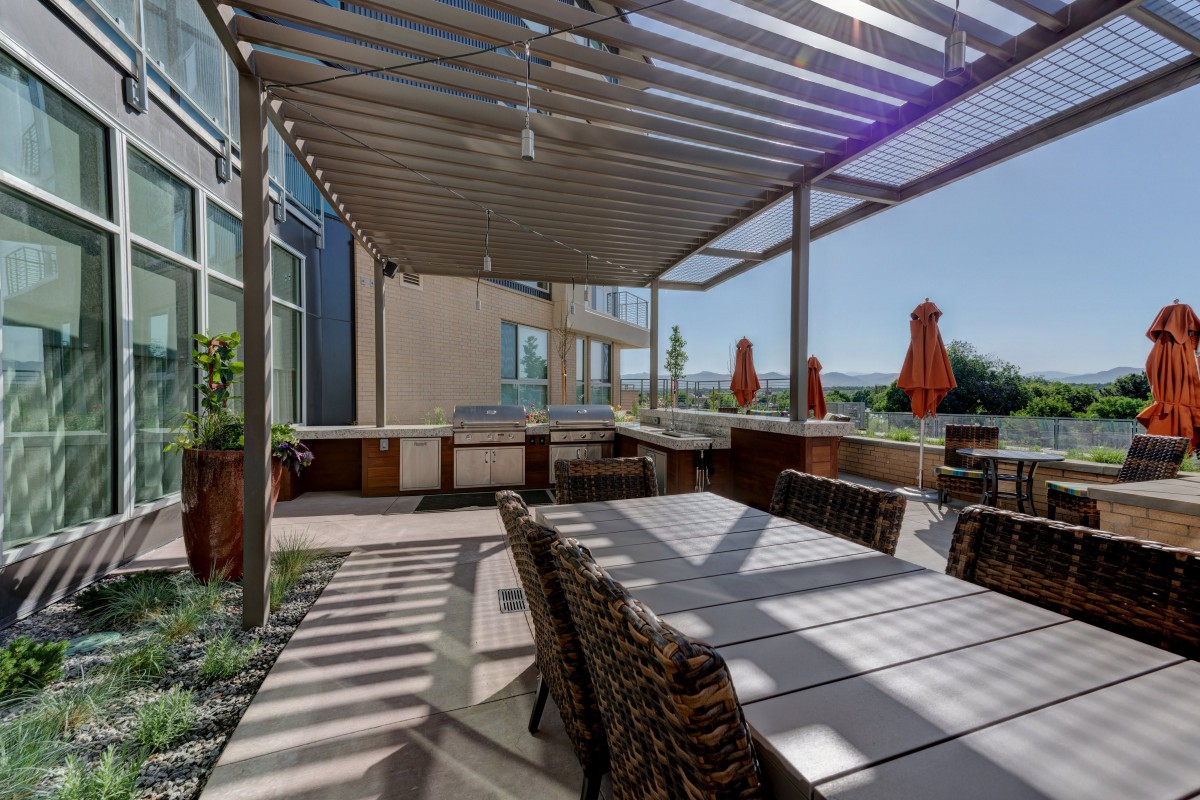 A modern outdoor patio with a pergola and dining area, featuring stylish furniture and surrounded by sunlight.