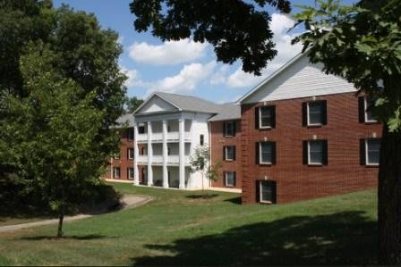 A brick dormitory building on a college campus surrounded by trees under a blue sky.
