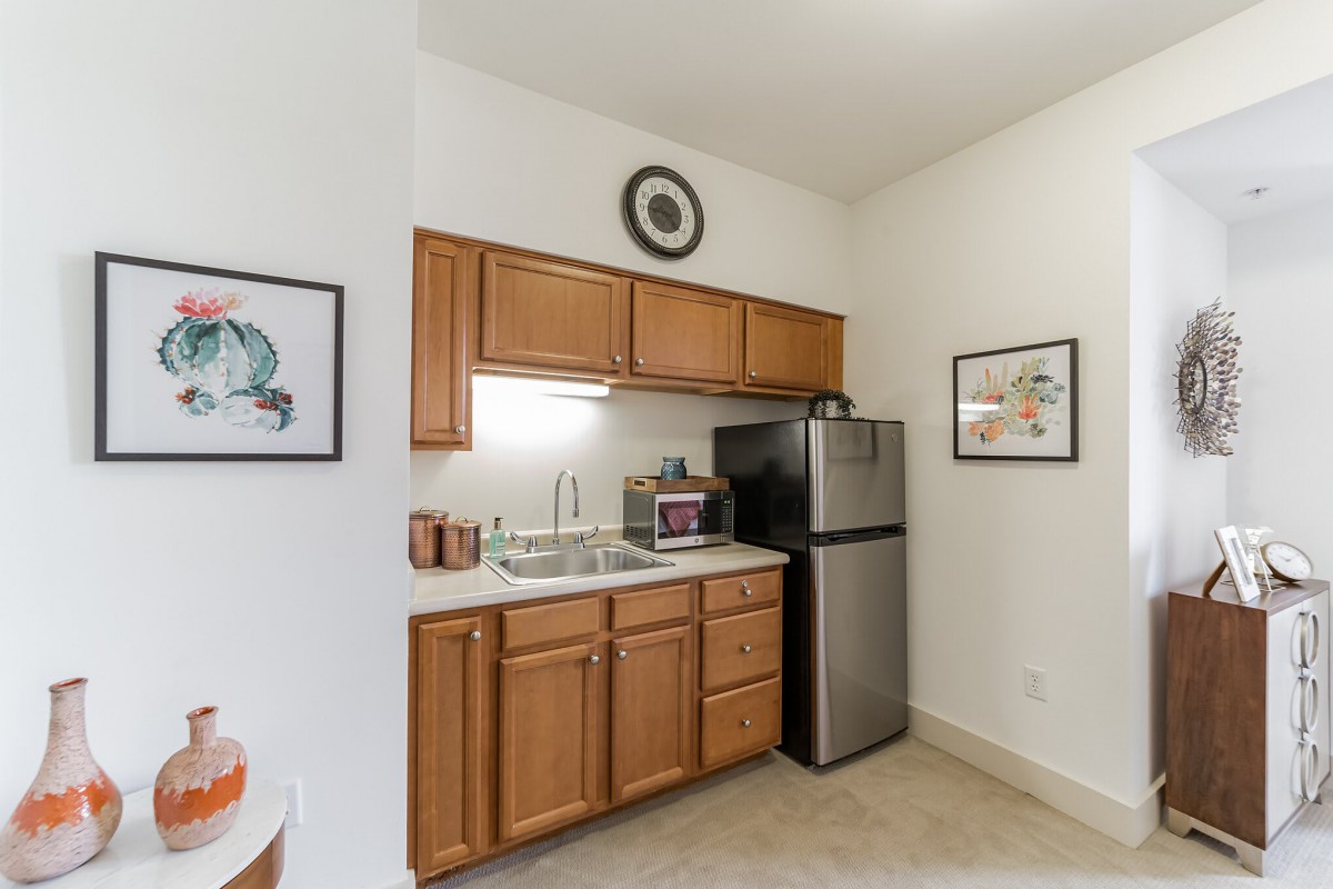 A compact kitchen with wooden cabinets, a sink, and a refrigerator, decorated with wall artwork.