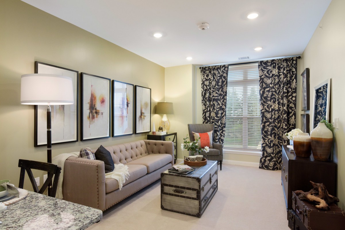A cozy living room featuring elegant decor with framed artwork, a tufted sofa, and patterned curtains.