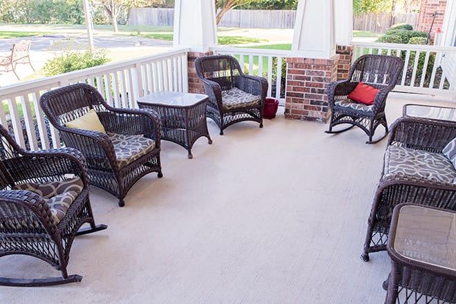 A cozy porch with wicker chairs and a small table, surrounded by a brick wall.