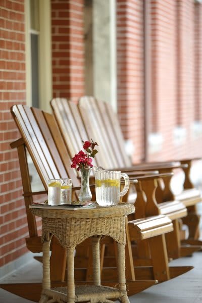 A cozy front porch with wooden rocking chairs, a table with lemonade, and flowers creating a welcoming atmosphere.