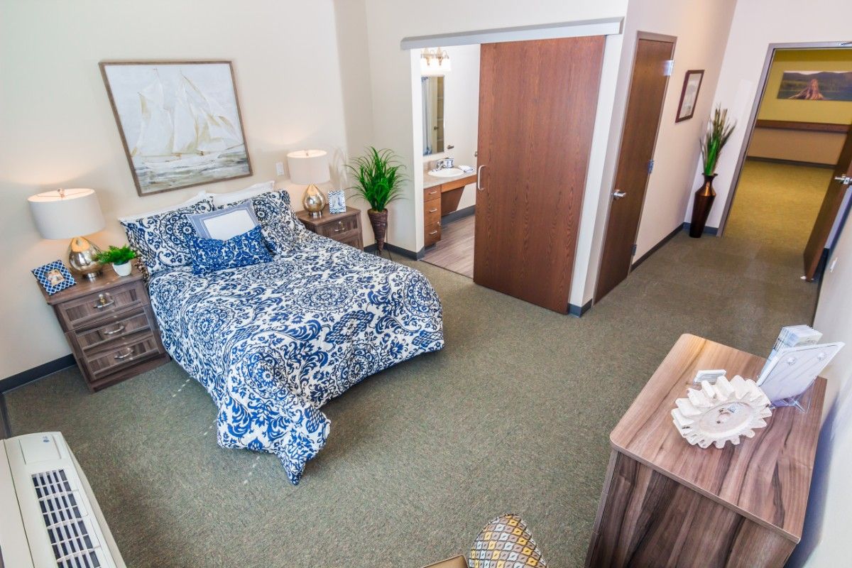A cozy bedroom with a blue patterned bedspread and an adjoining bathroom.