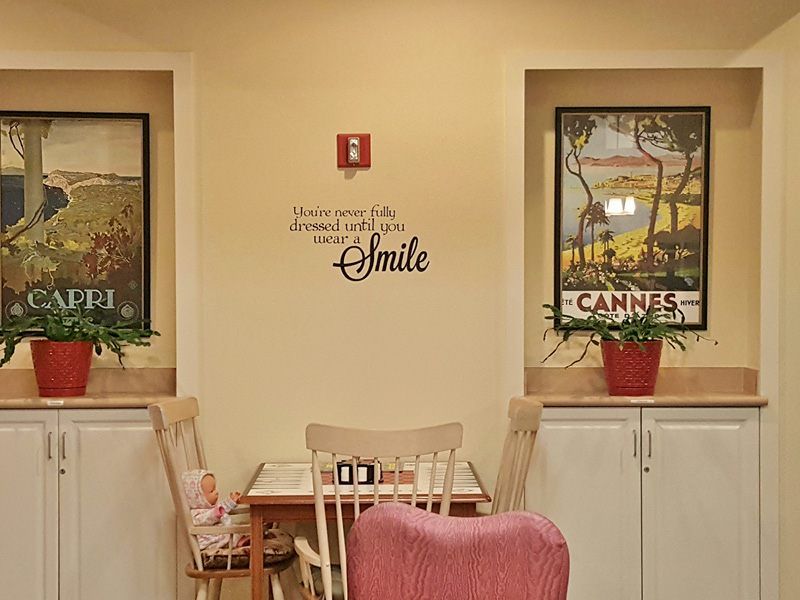 A cozy dining area with a small table set, wall art, and plants, featuring an inspirational quote.