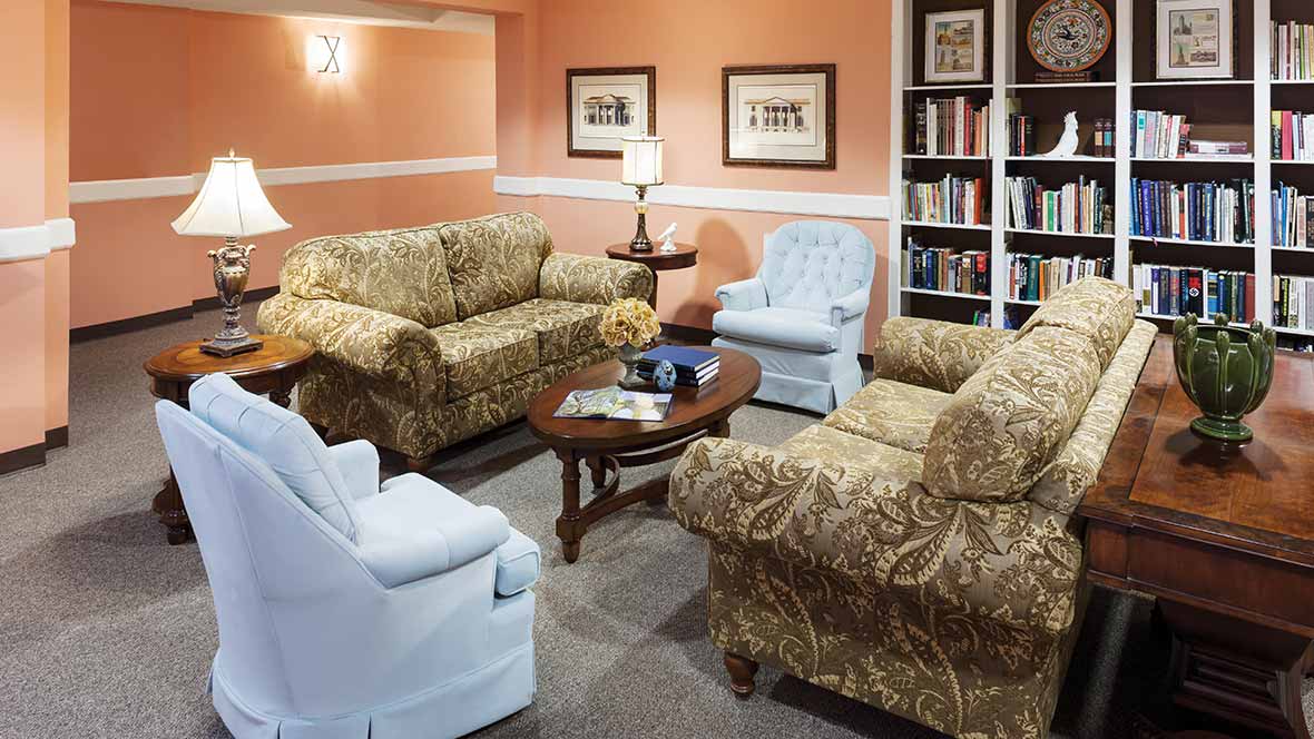 A cozy living room with patterned sofas and armchairs, a wooden coffee table, and a bookshelf.