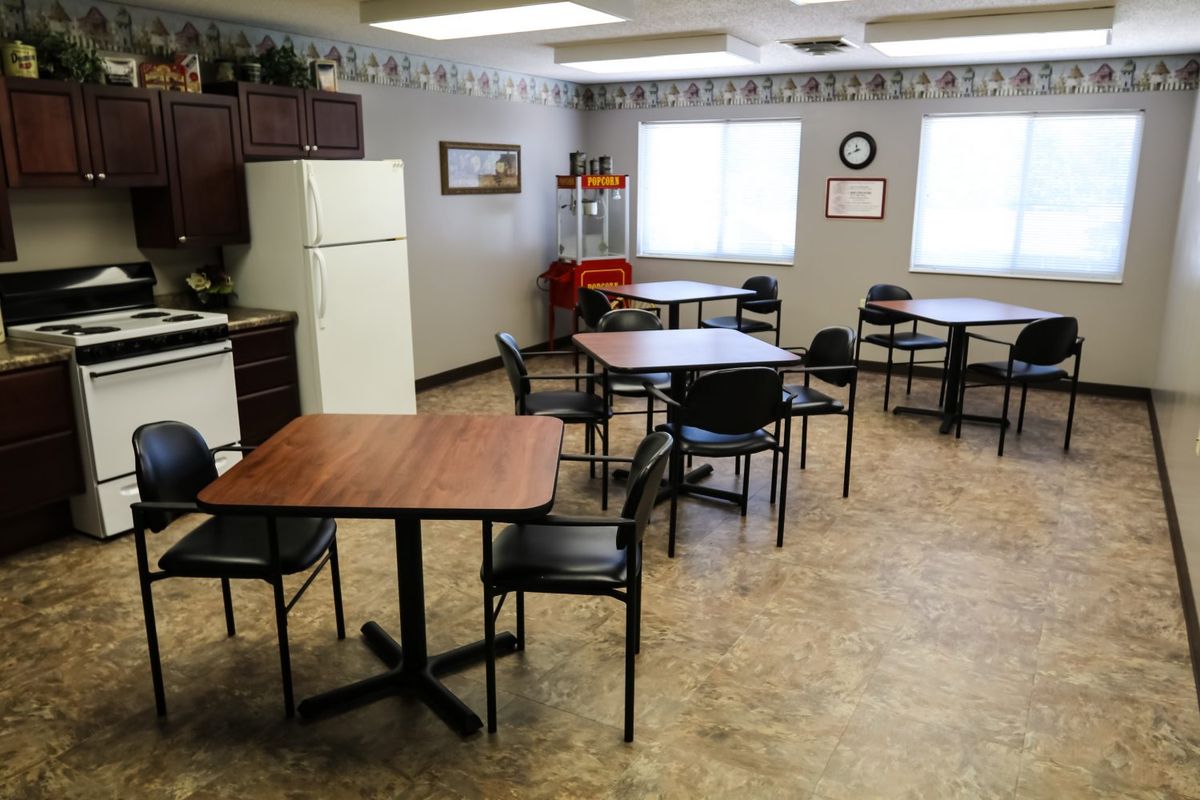 An empty cafeteria with tables, chairs, and a kitchenette area.
