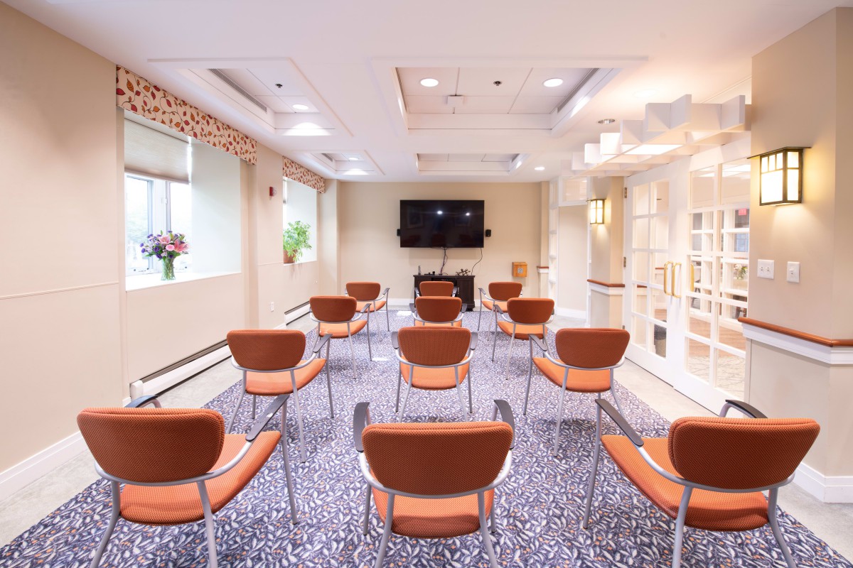 A well-lit conference room with neatly arranged chairs facing a television.