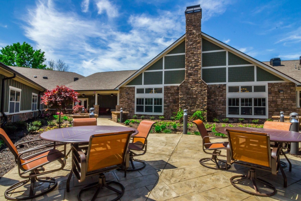 A spacious patio area with tables and chairs in front of a house with a chimney, set against a clear blue sky.