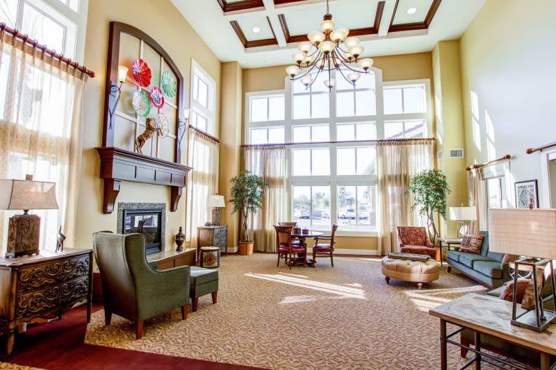 A spacious and well-lit living room featuring high ceilings, a chandelier, and large windows, complemented by comfortable furniture and a fireplace.