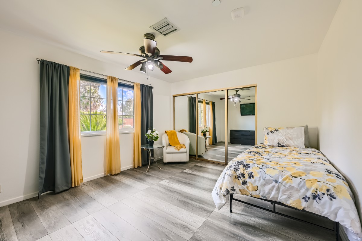 A modern bedroom featuring mirrored closet doors, a ceiling fan, and stylish decor with hardwood flooring.
