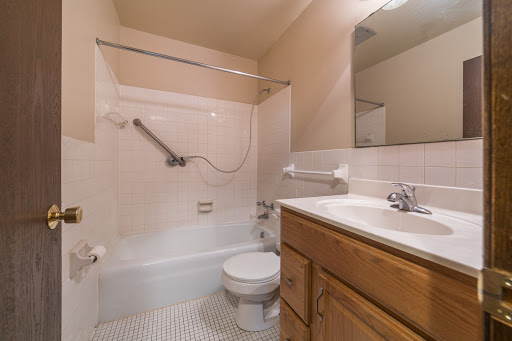 A compact bathroom featuring a bathtub with a shower, toilet, and wooden cabinetry.