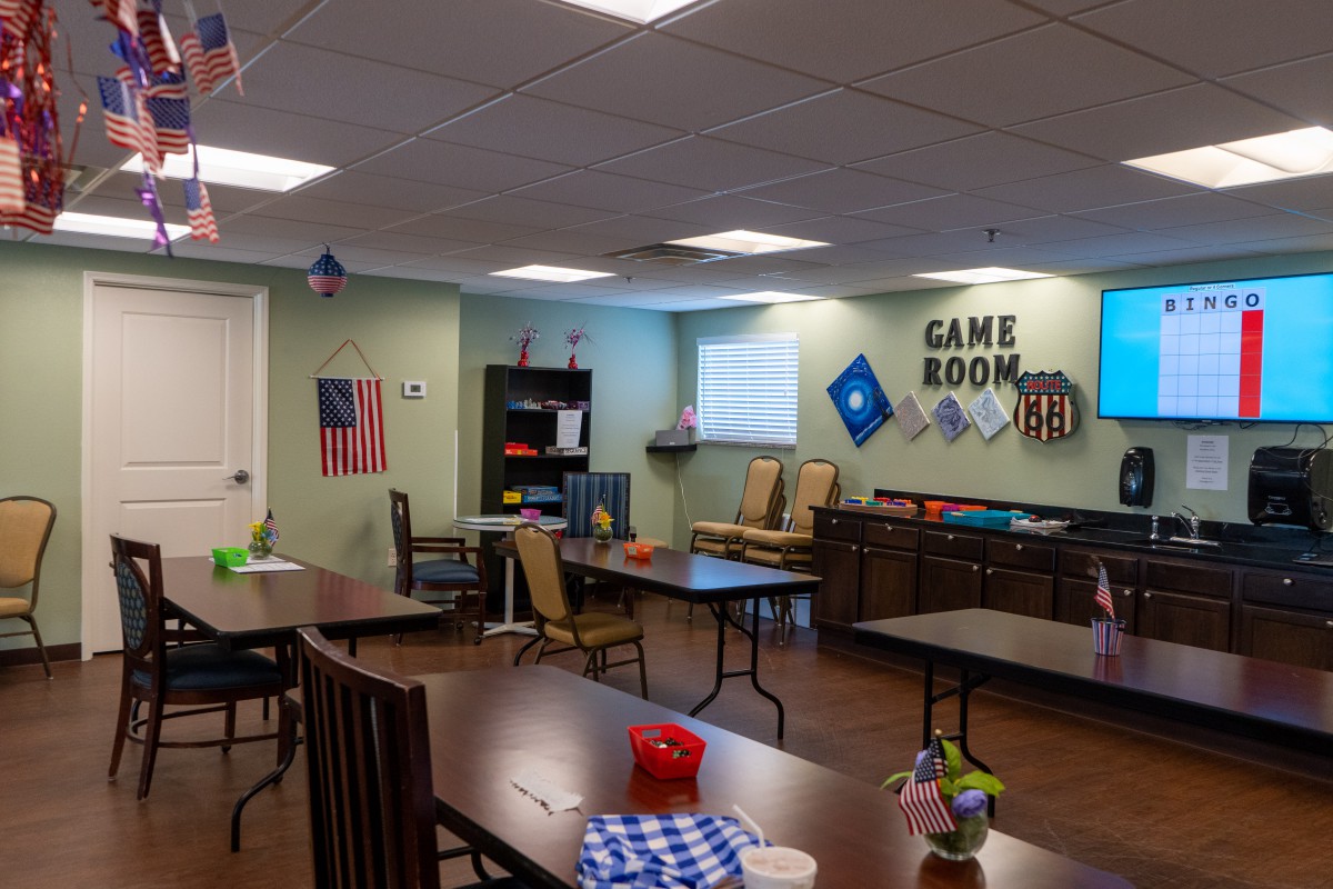 A spacious game room with tables and chairs, featuring colorful decorations and a prominent American flag on the wall.