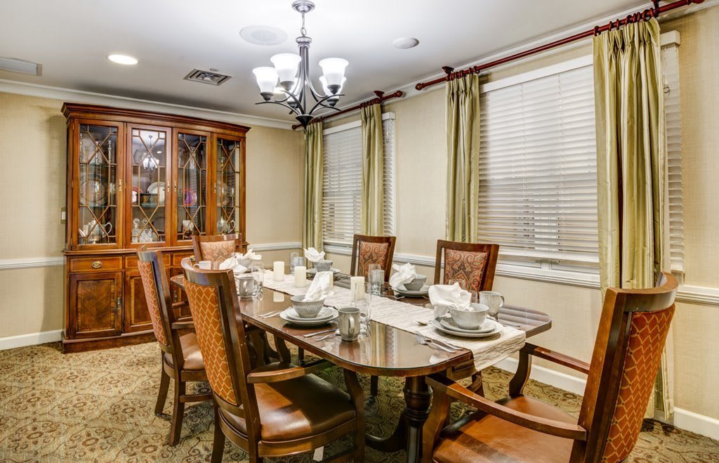 A classic dining room with a wooden table set for a meal, surrounded by chairs and illuminated by a chandelier.
