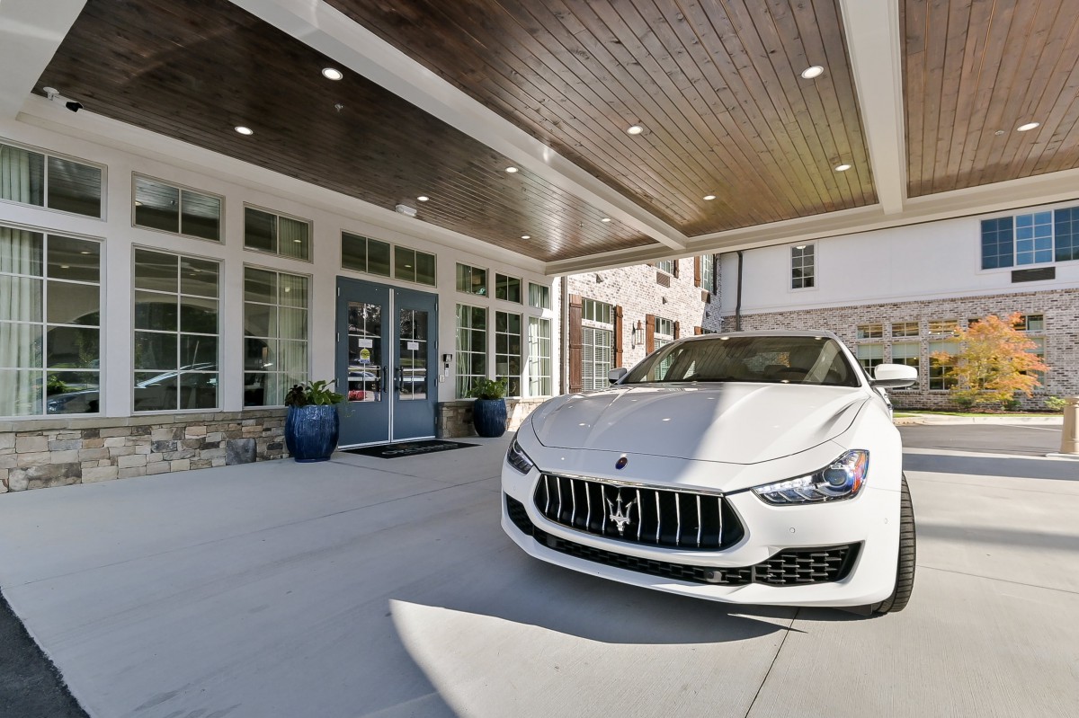 A luxury white Maserati parked at the entrance of a modern building.
